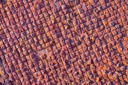 Chequered pattern of repetitive small squares on old rusty metal plate in beautiful warm sunset light.