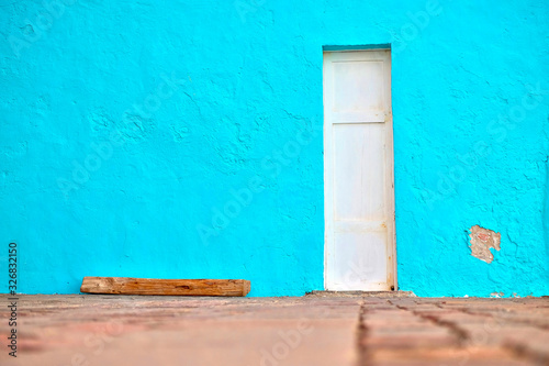 Narrow white door in a simple blue wall. Minimal Mediterranean village architecture detail. © Daguimagery