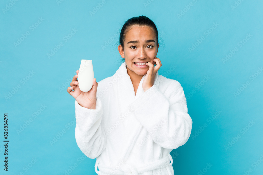 Young mixed race indian holding a moisturizer biting fingernails, nervous and very anxious.