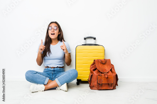 Young mixed race indian woman ready to go to travel pointing upside with opened mouth.
