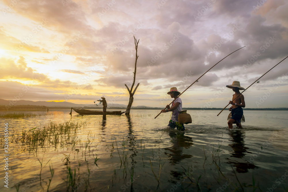 Asian boy and girl walking holding a fishing hook in the early morning. His uncle casting a net for catching freshwater fish on wooden boat in neighboring. Concepts nature and way of life.