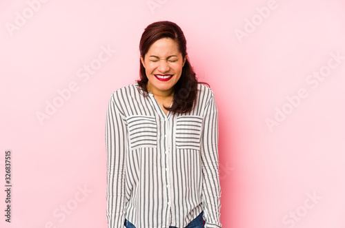 Middle age latin woman isolated on a pink background laughs and closes eyes, feels relaxed and happy. © Asier