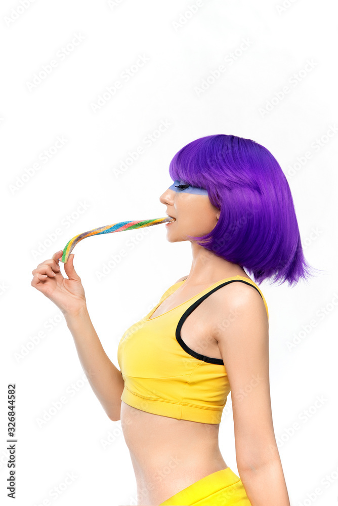 Studio shooting of a girl in a purple wig. The girl smiles playfully and holds a candy on a white background Studio shooting of a girl in a purple wig. The girl smiles playfully and holds a candy on a white background