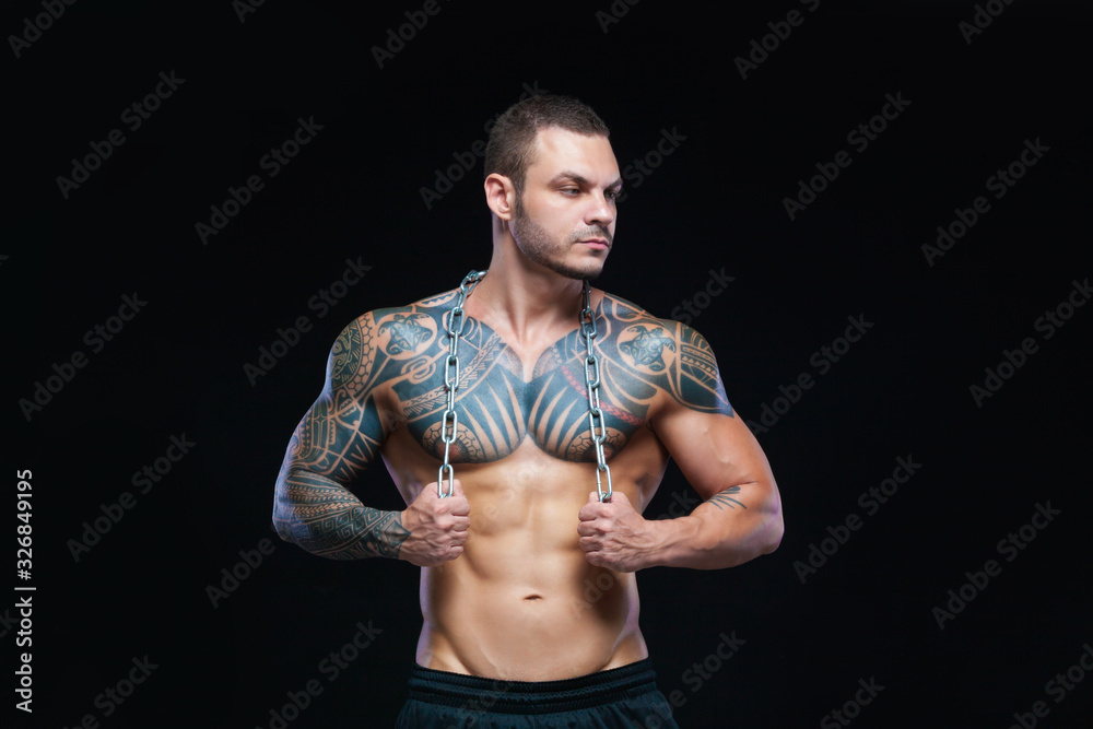 Fototapeta premium Tattooed strong muscular athletic man holding metal chain over his neck on black background