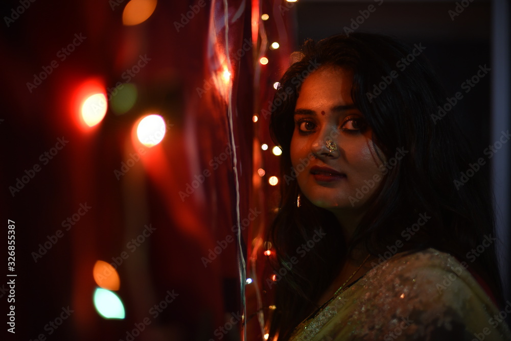 Portrait of an Indian Bengali beautiful brunette woman holding tiny colorful chain lights creating beautiful bokeh in the evening of Diwali. Indian lifestyle and religion. Portrait of an Indian Bengali beautiful brunette woman holding tiny colorful chain lights creating beautiful bokeh in the evening of Diwali. Indian lifestyle and religion.