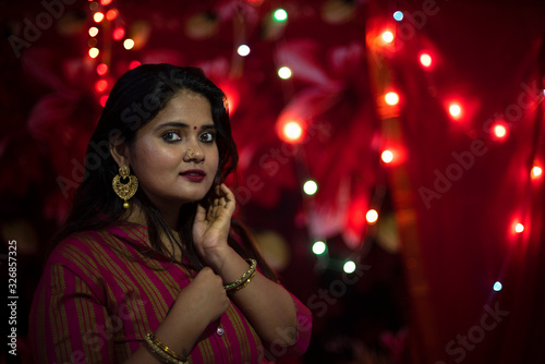 Portrait of an Indian Bengali beautiful brunette woman in front of the colorful light bokeh background created by tiny chain lights in the evening of Diwali. Indian lifestyle and religion.