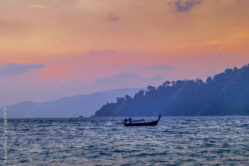 Sea view evening of a long-tail boat running in the sea with red sun light in the sky background, sunset at Lipe island, Satun, southern Thailand.