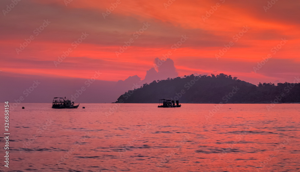 Sea view evening of the ships floating in the sea with island and red sky background, Twilight at Lipe island, Satun, southern Thailand.