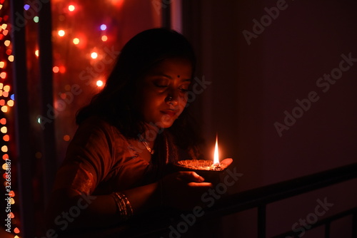 Two young and beautiful Indian Bengali women in Indian traditional dress are celebrating Diwali with diya/lamp and fire crackers on a balcony in darkness. Indian lifestyle and Diwali celebration