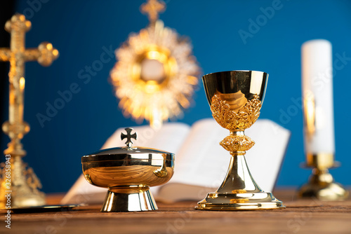 Catholic religion concept. Catholic symbols composition. The Cross, monstrance, Holy Bible and golden chalice on the altar. Blue background.