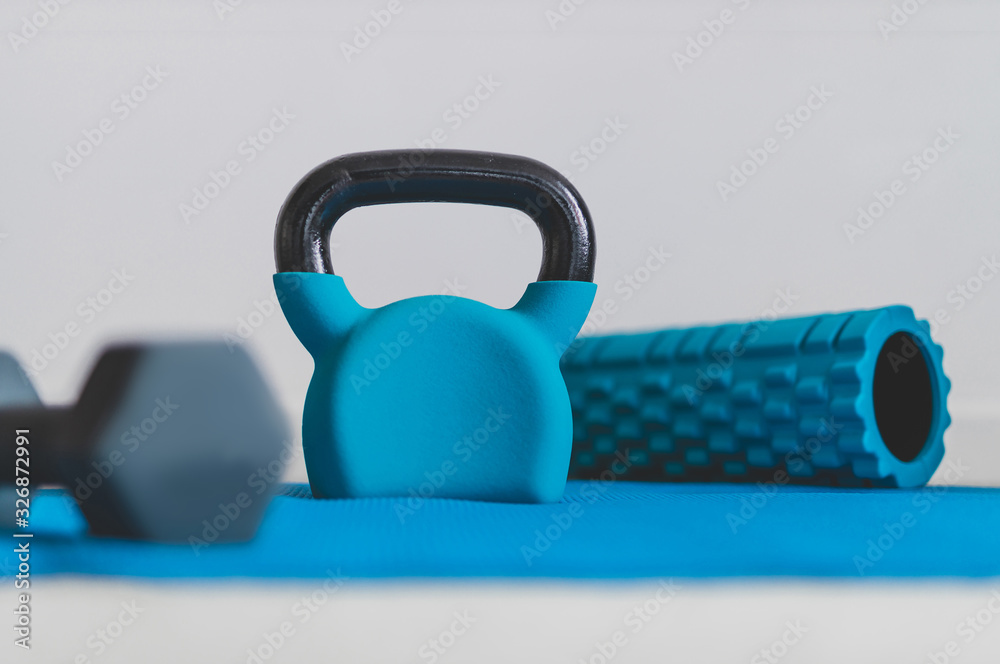 Obraz premium home gym concept, blue yoga mat with kettlebell foam roller and dumbbell shot at shallow depth of field from low perspective