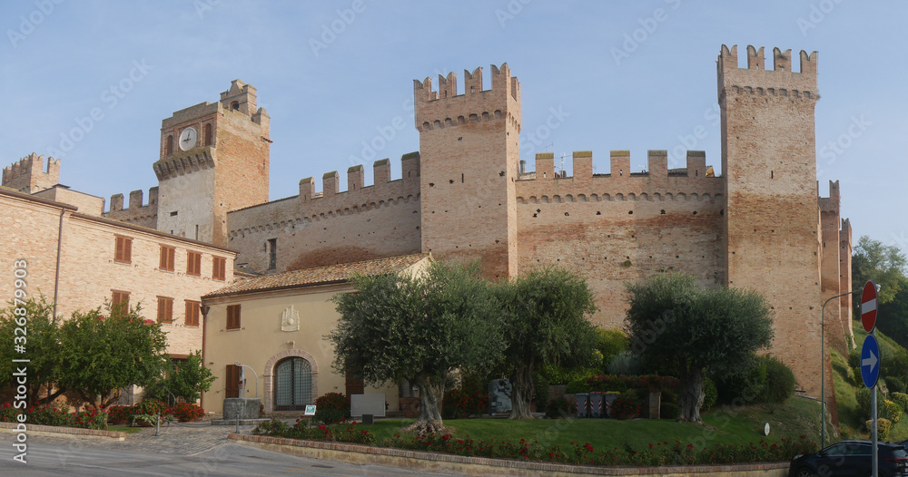 External walls with towers and laces around the village of Gradara with olive trees and green lawn.