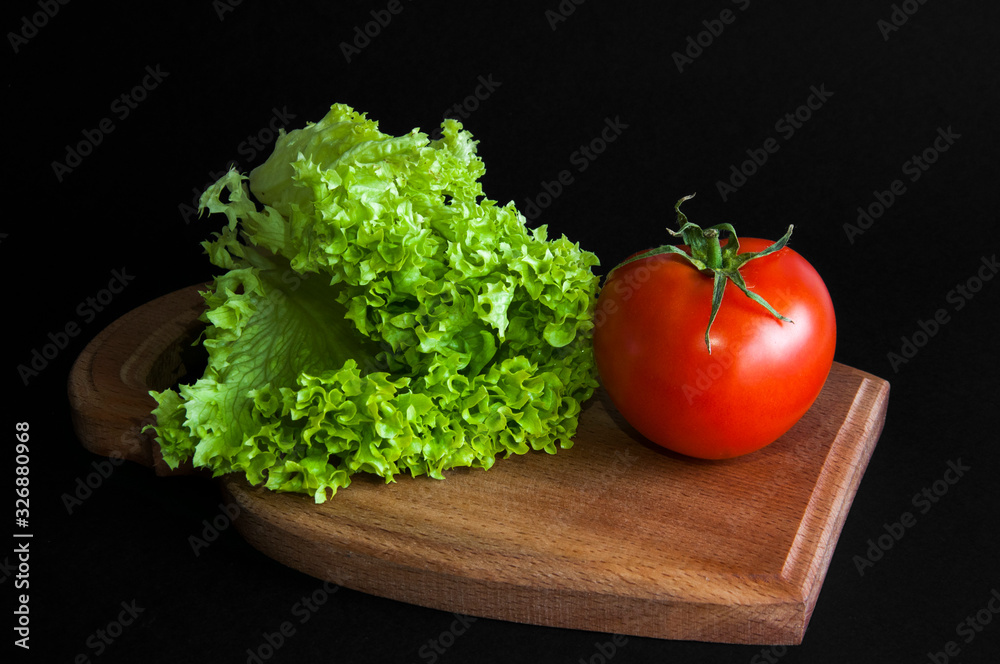 Lettuce leaves. Red tomato. On a wooden board. Black background Lettuce leaves. Red tomato. On a wooden board. Black background