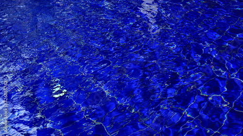 Background of swimming poll water with ripple and sun reflections on a surface.