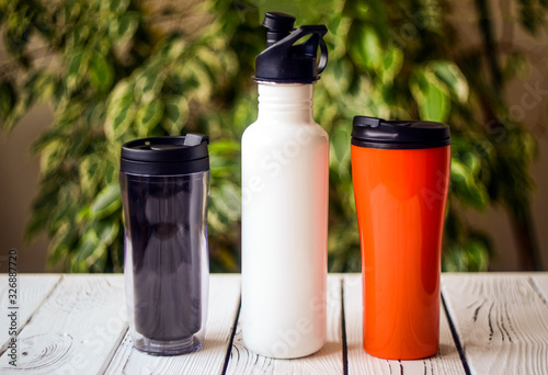 Assortment of refillable plastic and stainless steel water bottles on table against blurred background photo