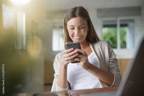 Cheerful woman at home using smartphone