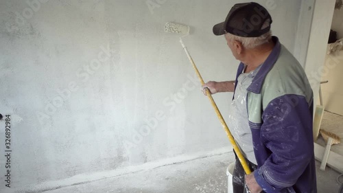 Senior painter painting the room white with roller, apartment redecoration