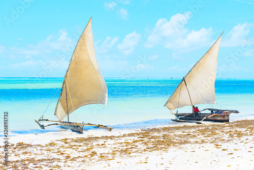 traditional African solid wood boats under sail on the shore of the Indian ocean with turquoise water on the island of Zanzibar, a concept of travel and summer