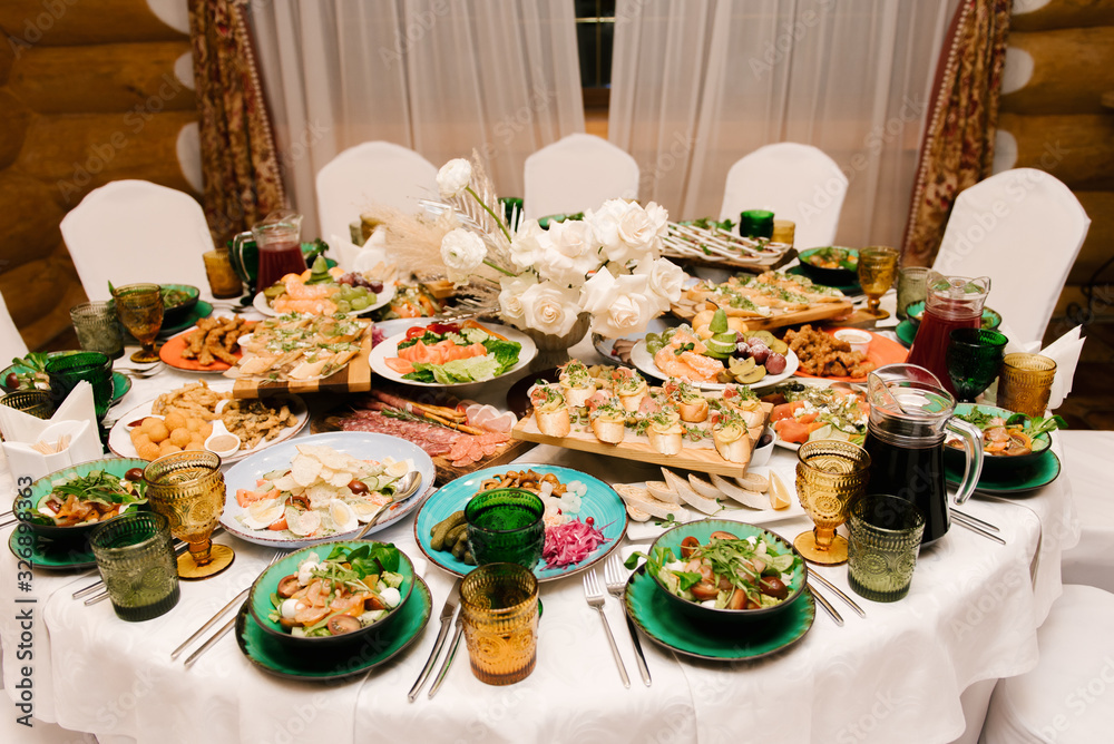 Fototapeta premium The round white table is filled with a large amount of food and various snacks in a luxurious interior, beautiful serving of the holiday table