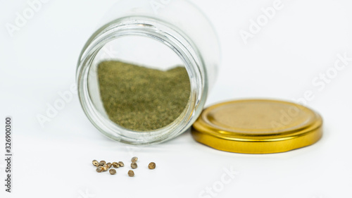 Close-up of glass jar with hashish and cannabis seeds isolated on white background.