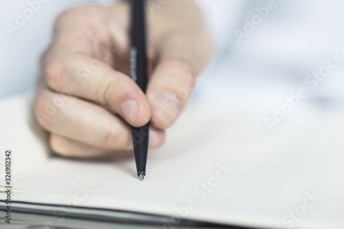 Man writes with a pen in notebook in a sunny office, business and education concept. Close up