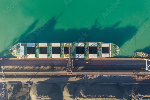 A bulk carrier stands at the berth of a coal terminal in the seaport, cargo is being loaded from an open warehouse onto a ship with a conveyor belt and a ship loading machine. photo