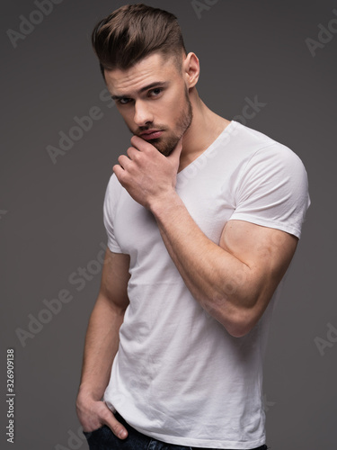 Portrait of a young man with a beard on a gray background. A muscular man in a t-shirt. Studio portrait. Fitness, fashion and beauty