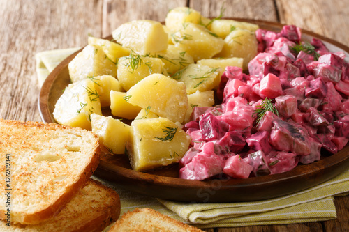 Tasty herring salad with vegetables and a side dish of boiled potatoes close-up in a plate. horizontal photo