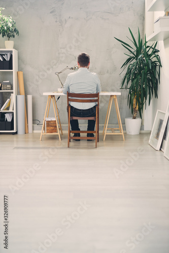 Back view of an young male architect sitting at his desk and typing.