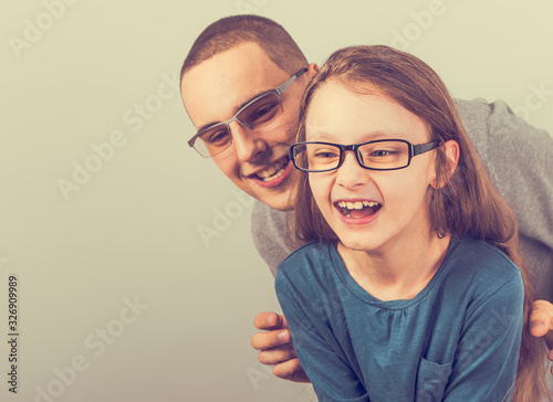 Happy young excited father and lauging joyful kid in fashion glasses hugging on empty copy space background with fun gesturing. Closeup photo