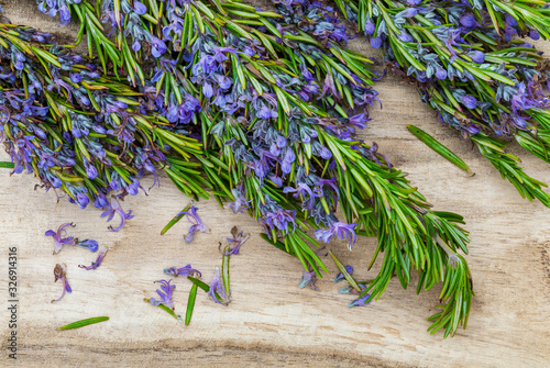 Bouquet of fresh rosemary and green with delicate purple flowers. On wooden background.
