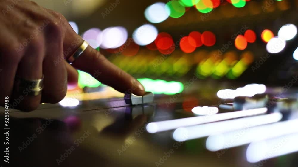 Audio Technician moving gently by finger button of TV Audio mixer on a live broadcasting event, blurry colorful background