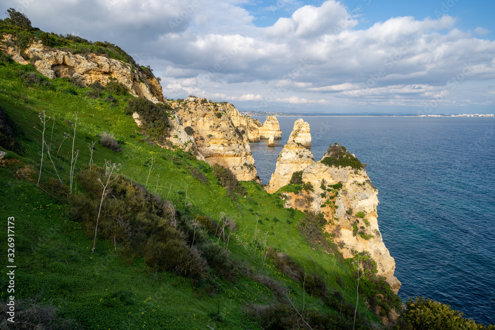 Steep, sloped natural cliff formations of Algarve coastline with green grass at Ponta da Piedade, in Algarve Portugal