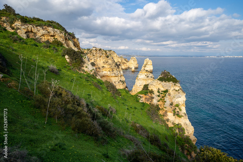 Steep, sloped natural cliff formations of Algarve coastline with green grass at Ponta da Piedade, in Algarve Portugal