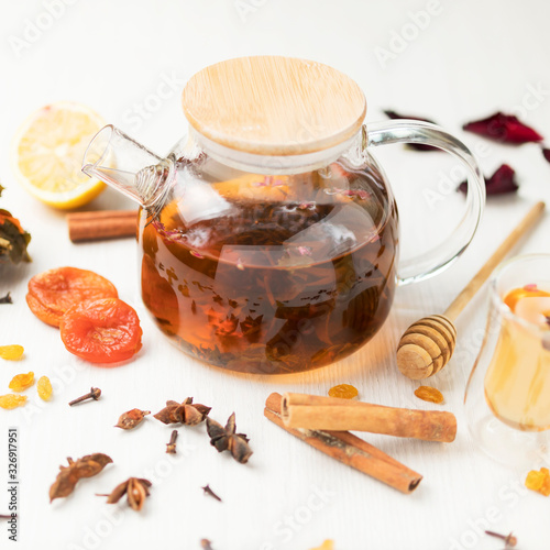 glass teapot with black tea on a white table with a composition of spices and dried fruits
