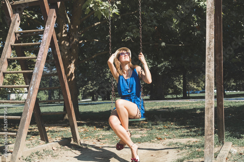 Cute young woman enjoying on a swing outdoors in summertime sunlight.