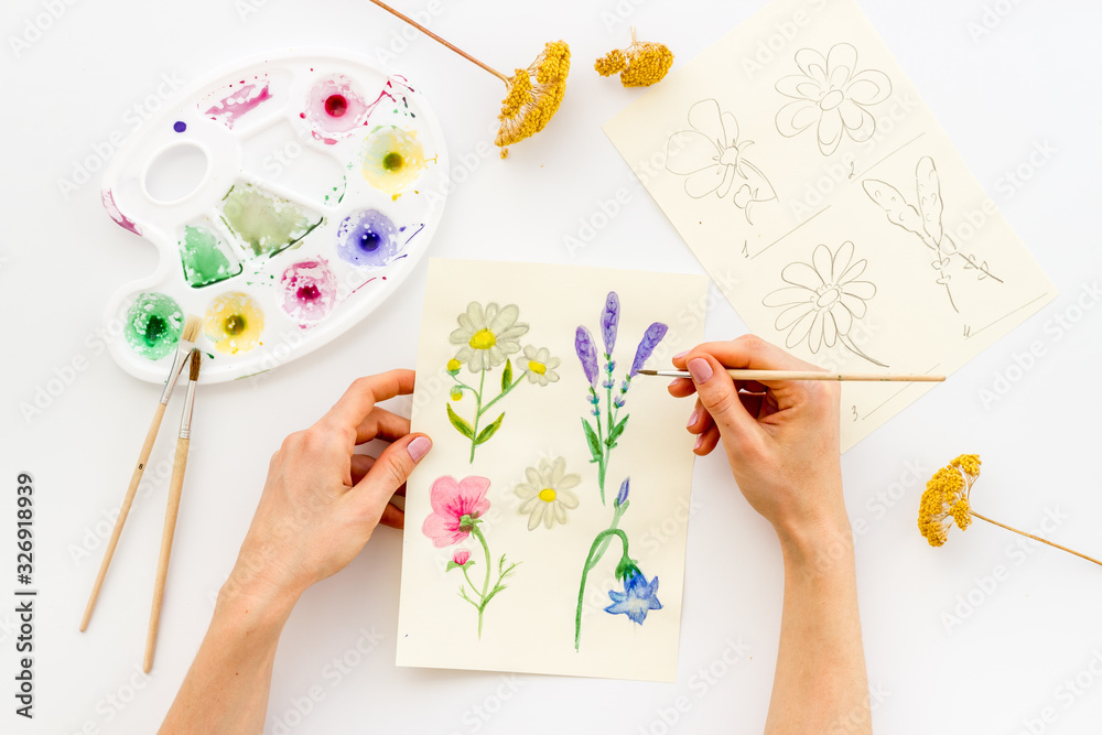 Painting. Female hands draw flowers on white background top-down Painting. Female hands draw flowers on white background top-down