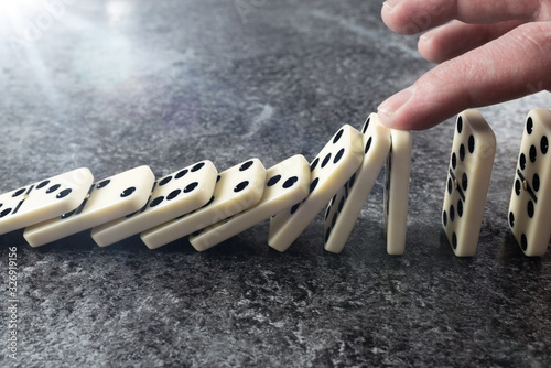 Obraz na płótnie close-up of male hand preventing line of domino tiles from toppling and falling,