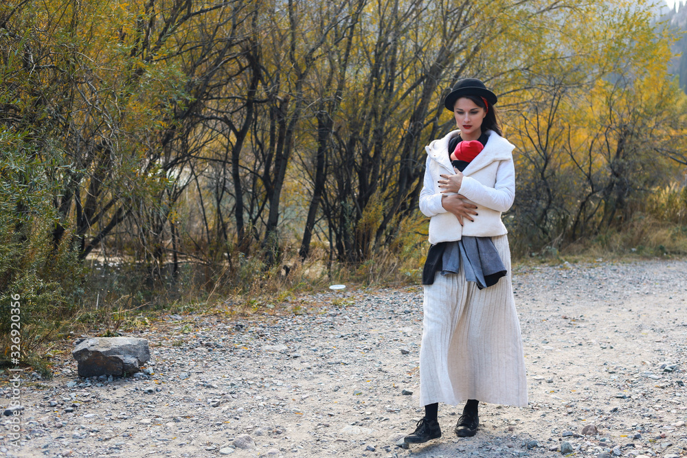 Beautiful young mother with her infant baby in sling outdoor. Mother is carrying her child and walk in autumn nature. Babywearing concept Beautiful young mother with her infant baby in sling outdoor. Mother is carrying her child and walk in autumn nature. Babywearing concept