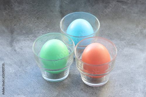 Three Easter eggs painted in pastel colors with glass cups on a gray background. Selective focus.