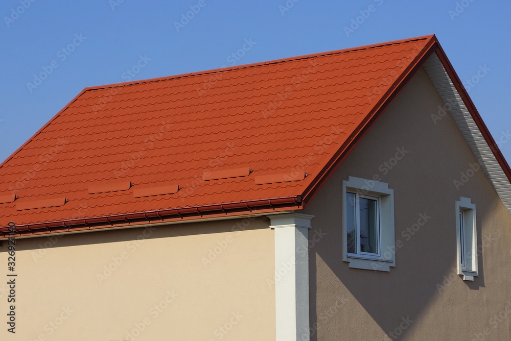 large private brown house with white windows under a red tiled roof against a blue sky on a sunny day
