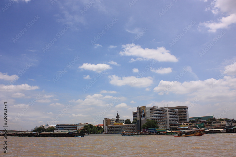 Chao Phraya River in brown colour with boats and Bangkok city old town with cloudy blue sky, with copy space.
