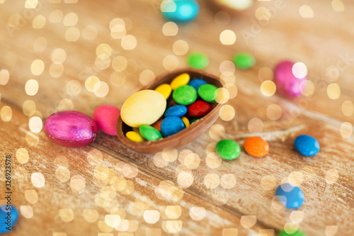 easter, sweets and confectionery concept - close up of chocolate egg and candy drops on wooden table