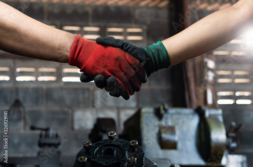 Male and female industrial workers shaking hands in factory workshop wearing protective workwear - Business and commercial teamwork within the workplace - Working together, goals and success concept