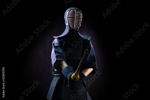 Kendo fighter in armor practicing with bamboo sword with bokuto on black background. Sports uniform