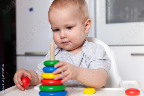 Adorable cute little baby is playing with colorful wooden pyramid