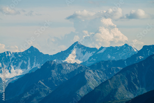 Atmospheric alpine landscape with giant low cloud above great glacier mountain with sunlight on snow. Big rocks and mountains under cloudy sky in sunny day. Awesome minimalist highland scenery.