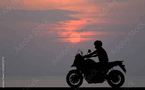 Silhouette biker with his motorbike beside the natural lake and beautiful sunset sky.