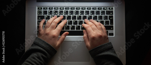 Overhead hacker in the hood working with laptop and mobile phone typing text in the darkroom. Russian hacker hacking the server in the dark. A hacker girl sitting in the dark with her laptop. Banner.