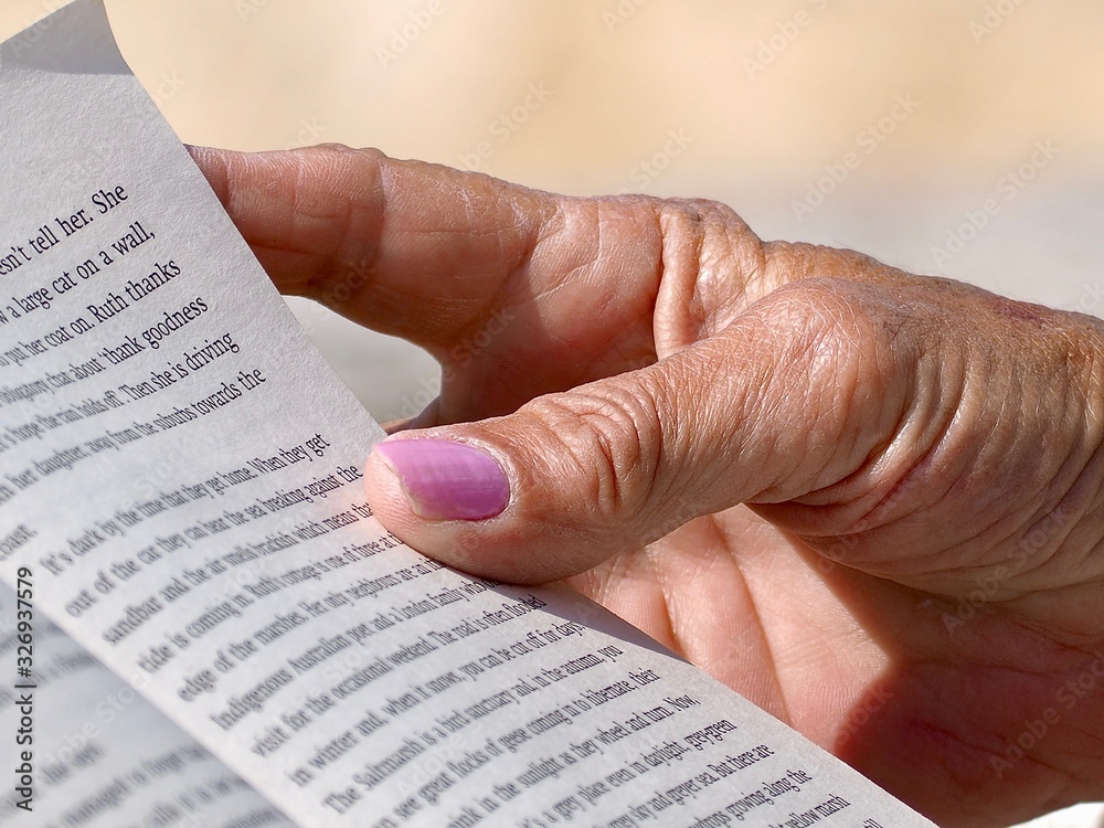 Obraz premium Closeup of a hand of an old Woman with pink fingernails reading